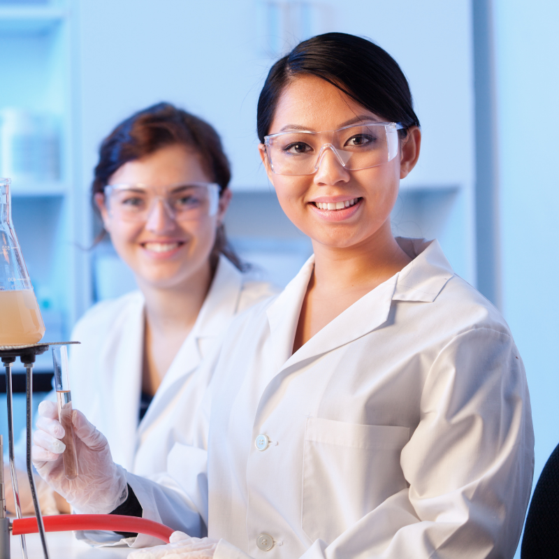 Two women in a laboratory looking at the camera holding a test tube